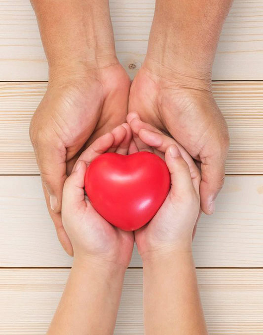 Two hands holding a red heart in front of them.